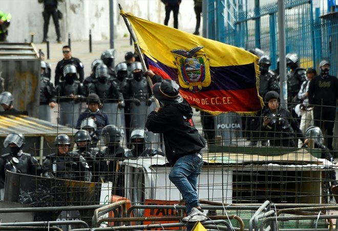 A protester waves the Ecuadorian flag as police stand guard around the National Assembly on June 25, 2022 in Quito.