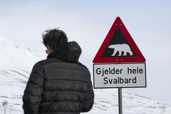 A man stands next to a polar bear warning sign at the side of a road near Longyearbyen on May 2, 2022, in the archipelago of Svalbard, northern Norway